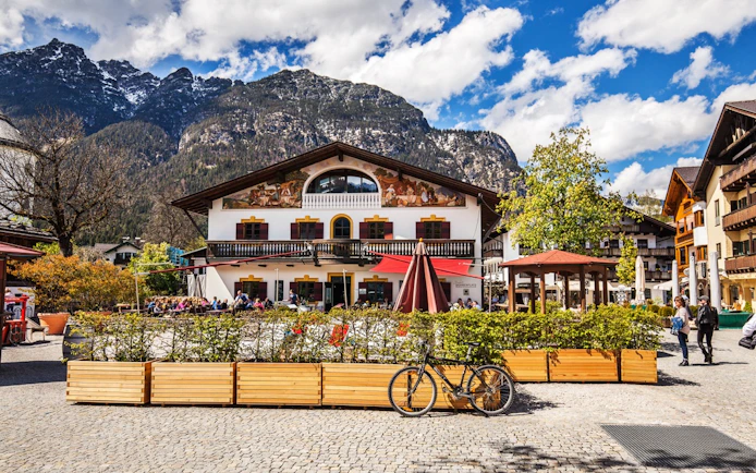 Bavarian building with frescoes in Oberammergau, Germany, set against mountain backdrop.