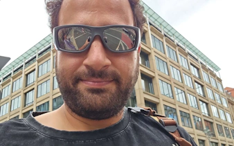 Man in sunglasses with cityscape reflection, Berlin exploration game.