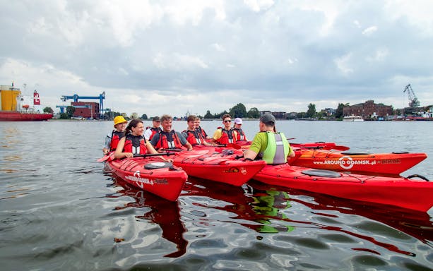 Group kayaking on the Motława River in Gdansk, Poland, with industrial backdrop.