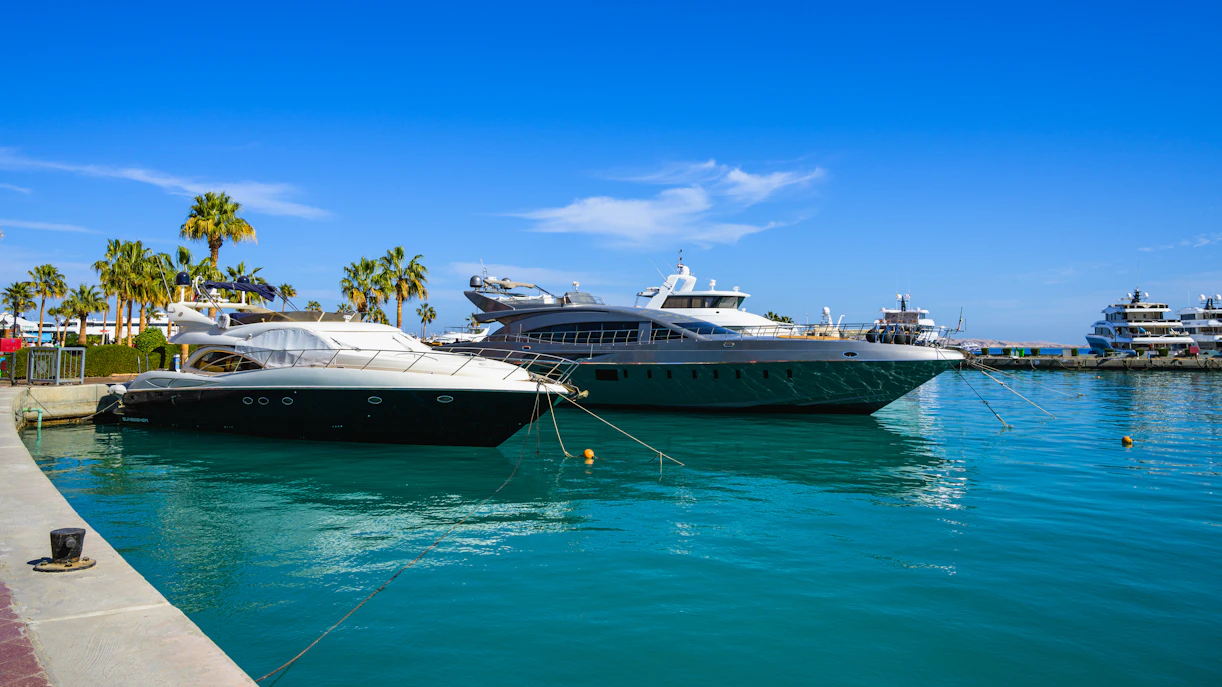 Yachts docked at Hurghada Marina with palm trees and clear blue sky.