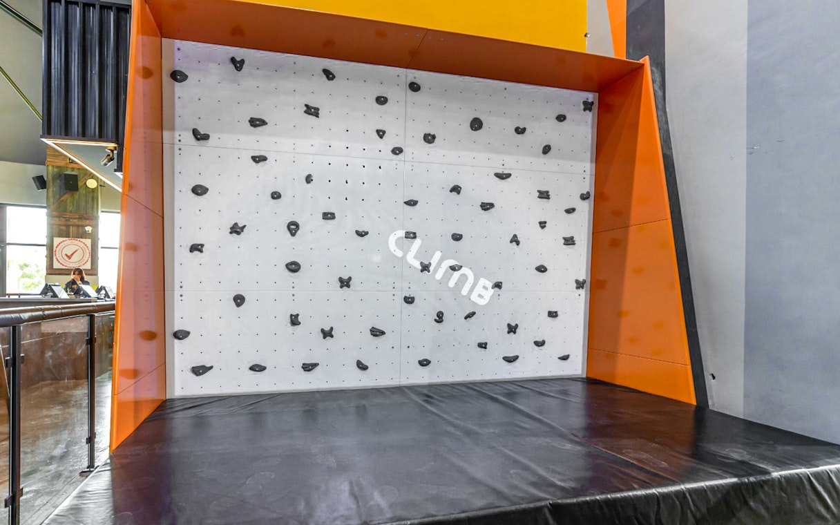 Indoor climbing wall at Adrenark Adventure with safety mat and climbing holds.