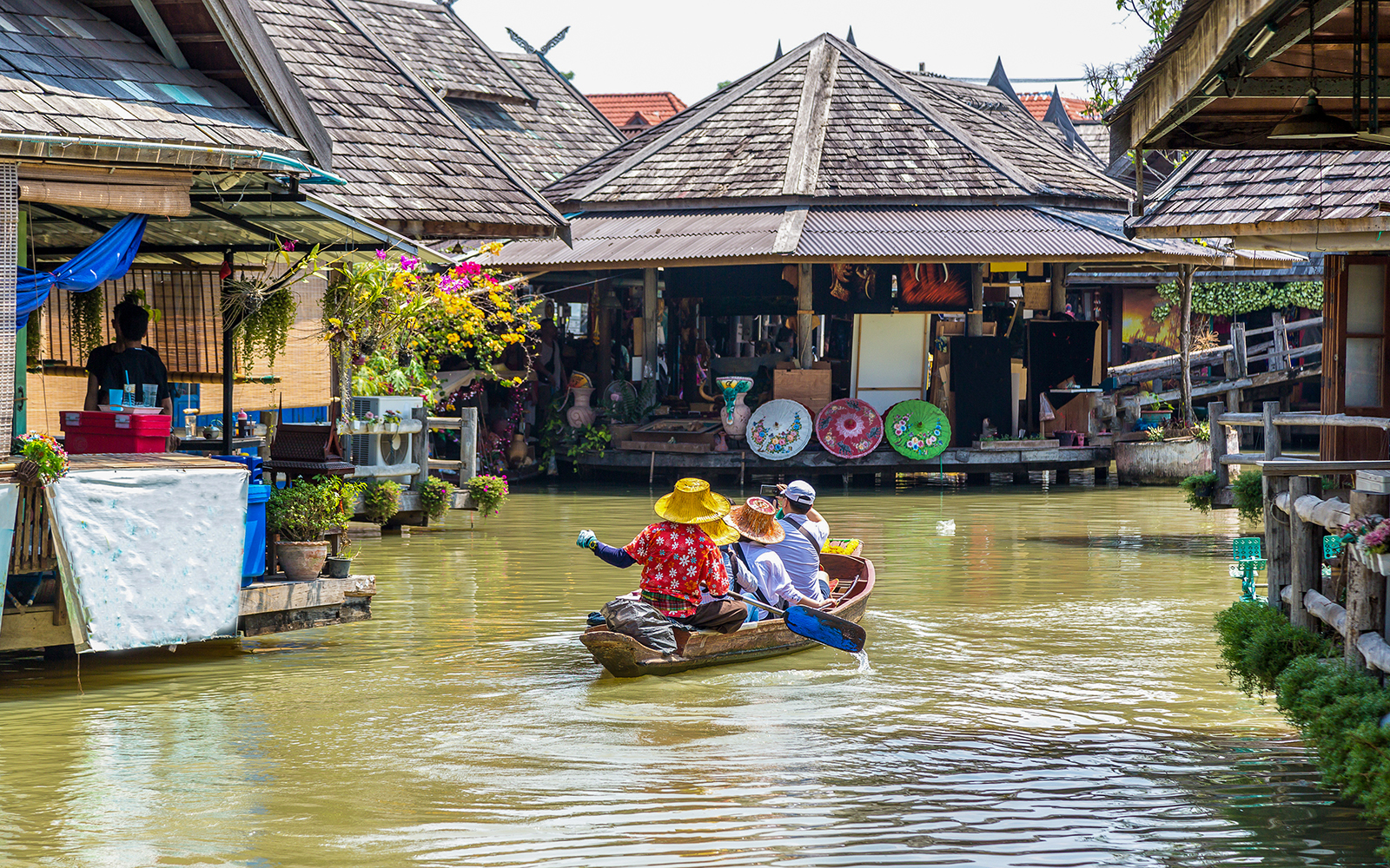 People exploring Pattaya Floating Market on a boat surrounded by colorful stalls and goods.