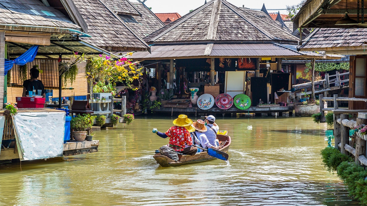 People exploring Pattaya Floating Market on a boat surrounded by colorful stalls and goods.