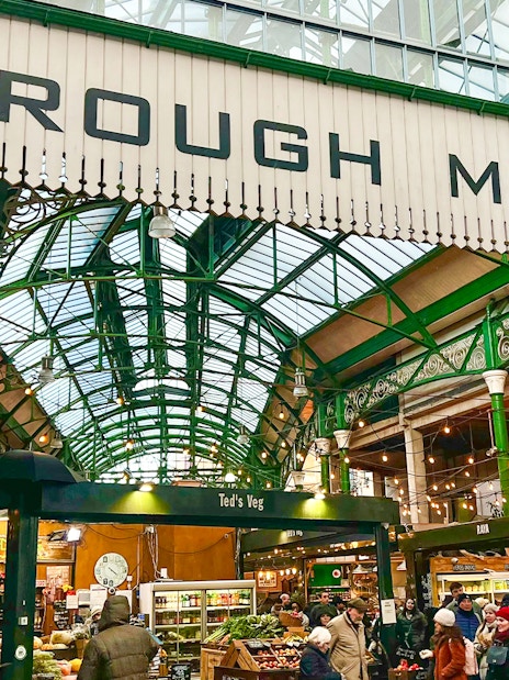 Borough Market entrance with visitors exploring food stalls in London.