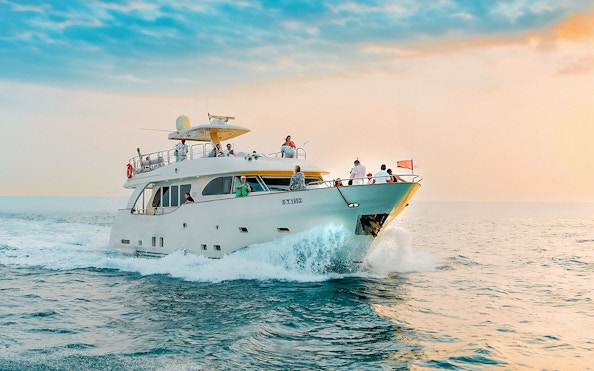 Yacht cruising on open water during sunset with passengers enjoying the view.