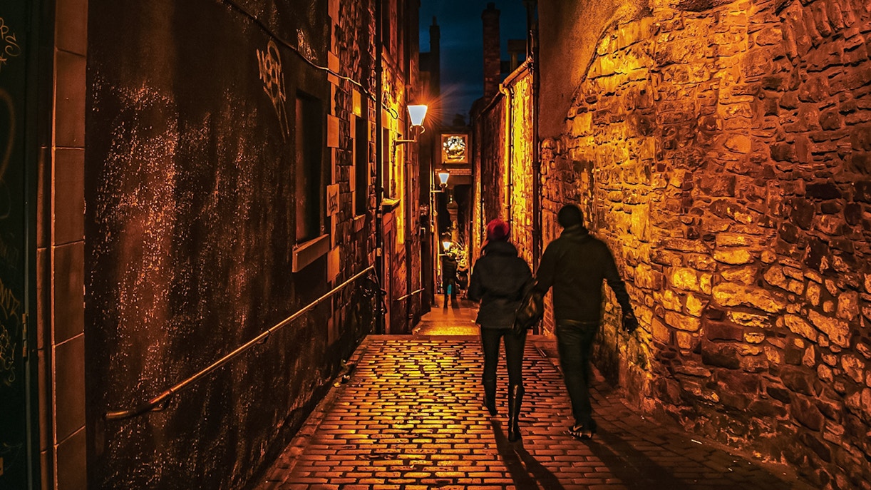 Couple walking through dimly lit cobblestone alley on Extreme Paranormal Activity Tour.