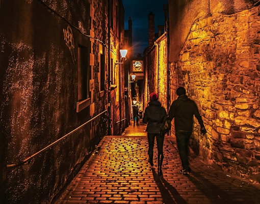Couple walking through dimly lit cobblestone alley on Extreme Paranormal Activity Tour.