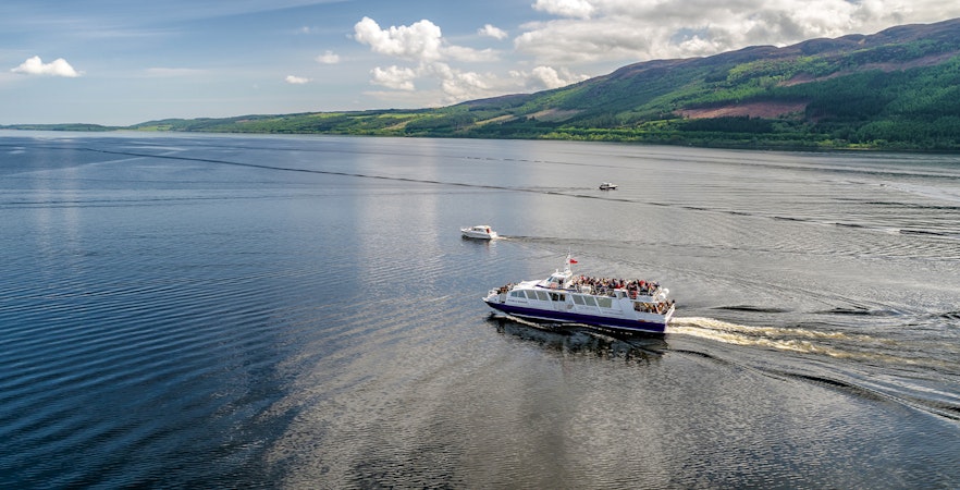 Cruise ship on Loch Ness, Scotland with scenic hills in the background.