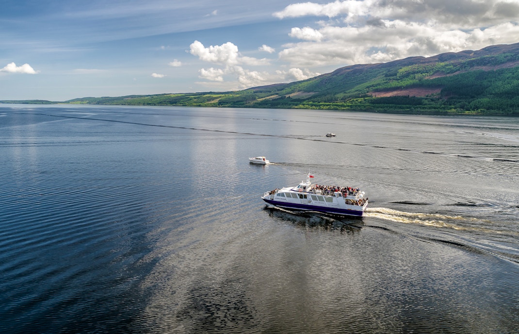 Cruise ship on Loch Ness, Scotland with scenic hills in the background.