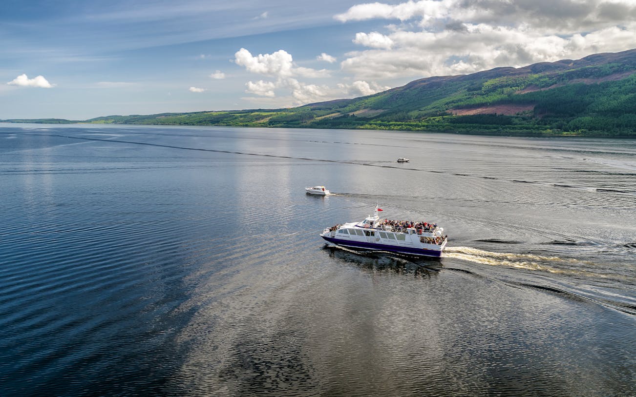 Cruise ship on Loch Ness, Scotland with scenic hills in the background.