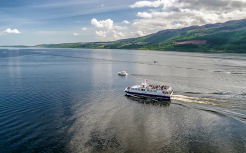 Cruise ship on Loch Ness, Scotland with scenic hills in the background.