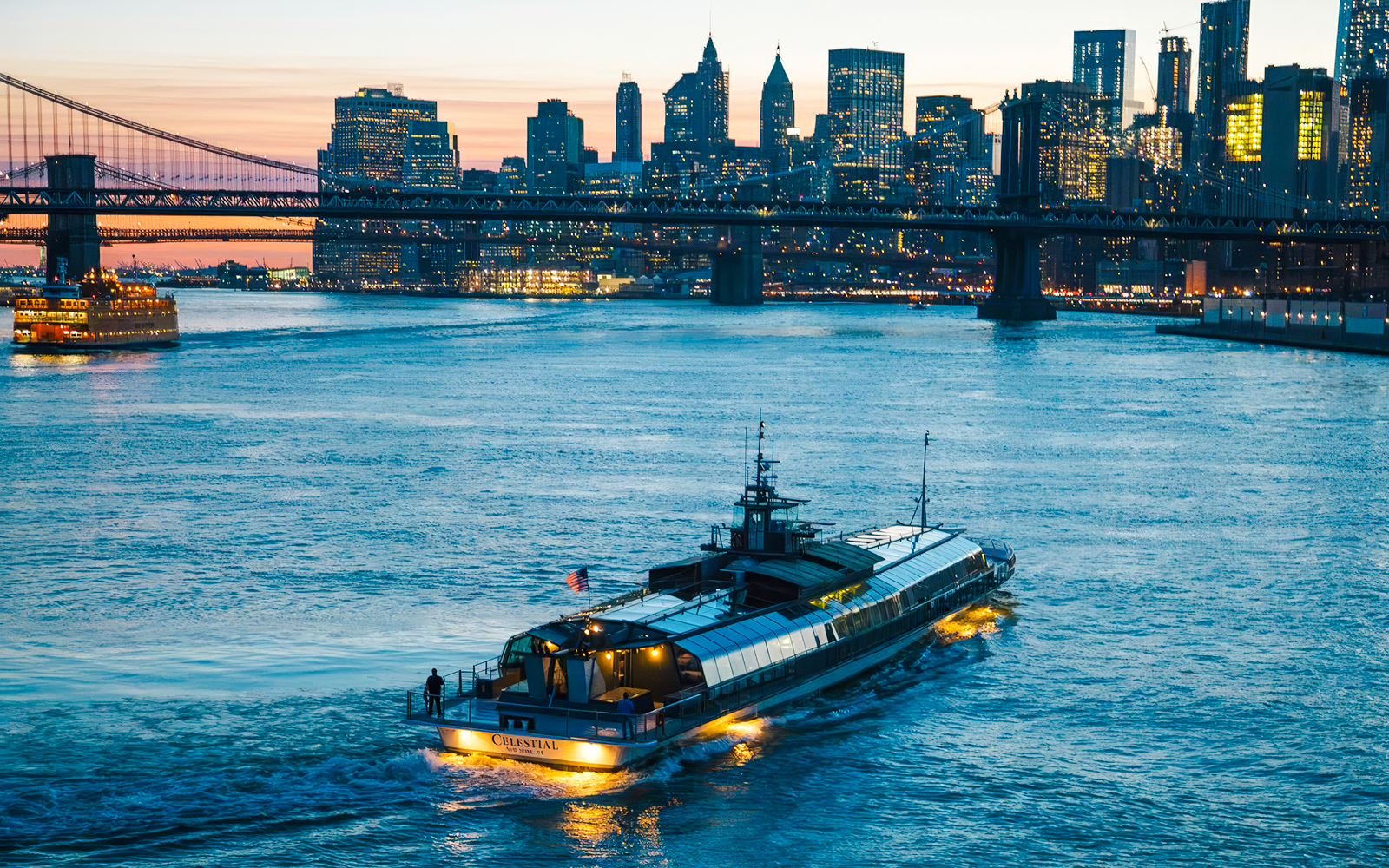 Dinner cruise boat on New York's East River with city skyline and bridge at sunset.