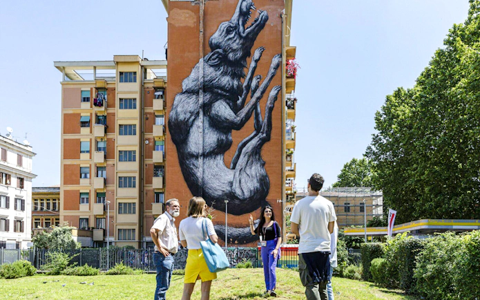 Tourists viewing street art mural on a building during Taste of Testaccio tour in Rome.