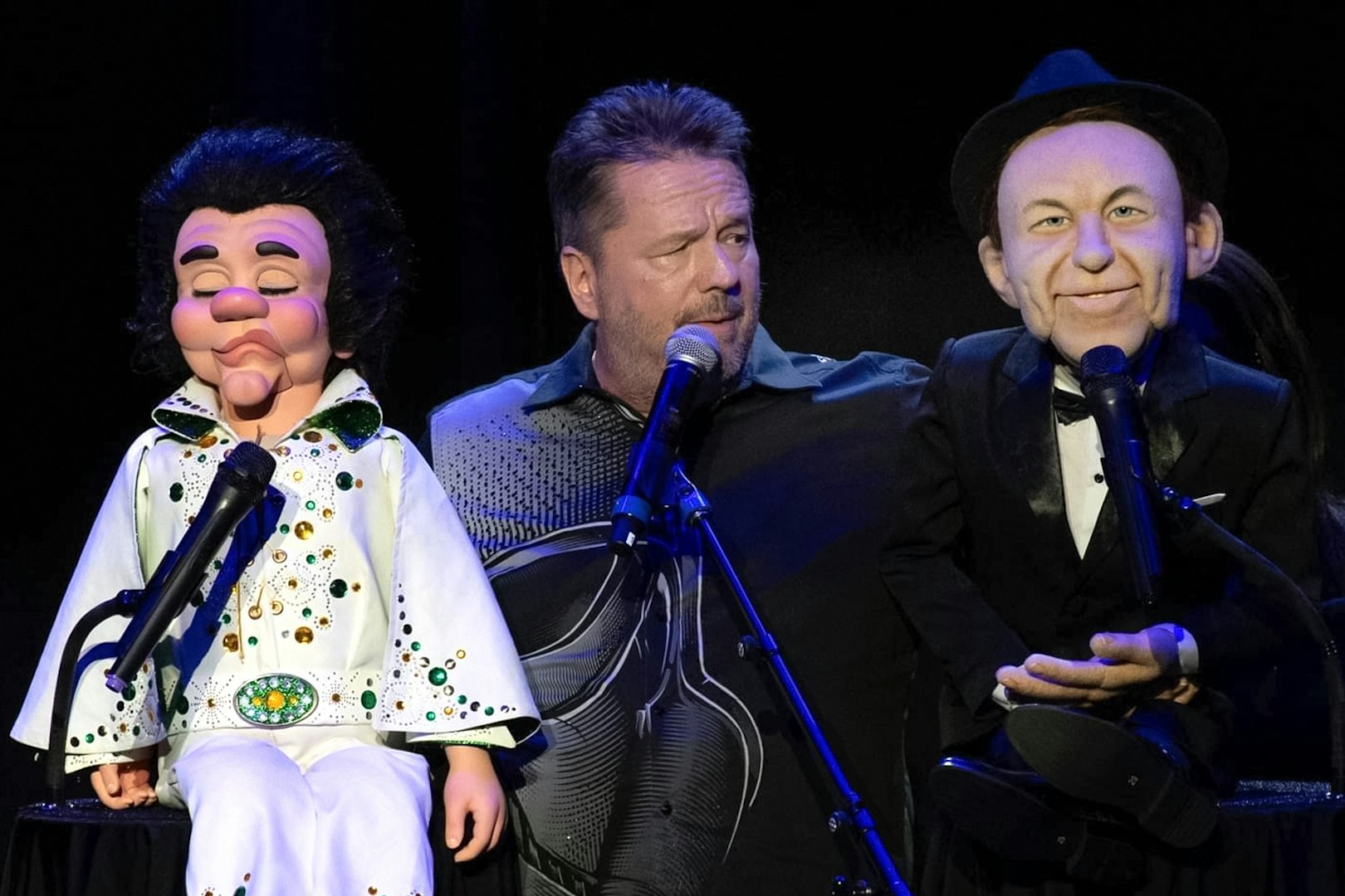 Ventriloquist performing with Elvis and Frank Sinatra puppets on stage.