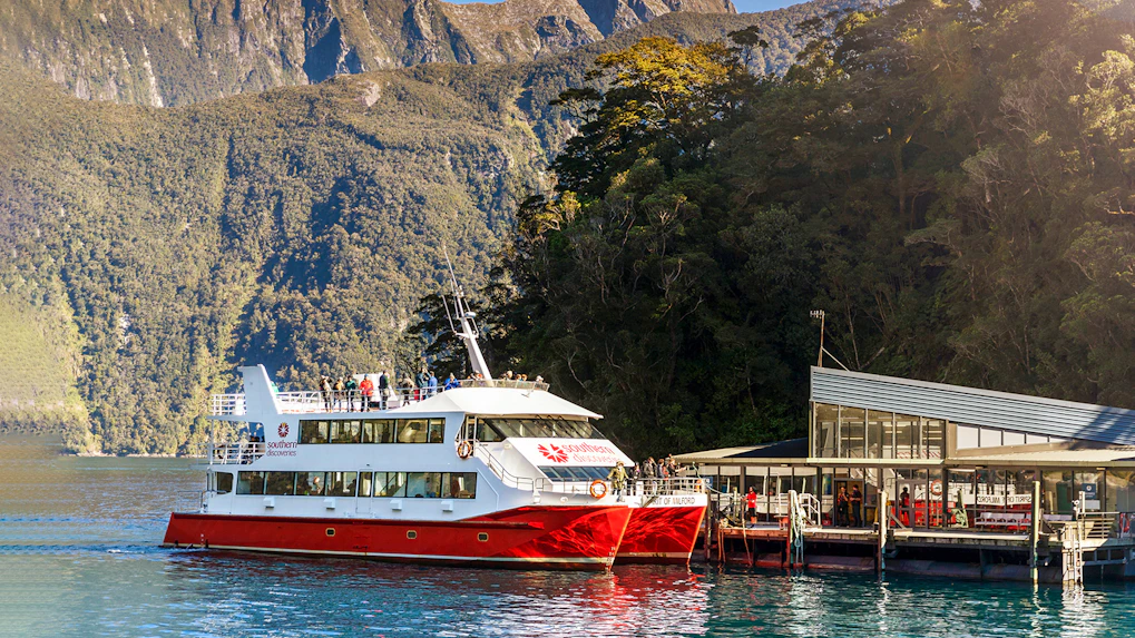 Cruise boat docked at Milford Sound with scenic mountain backdrop, Te Anau tour.