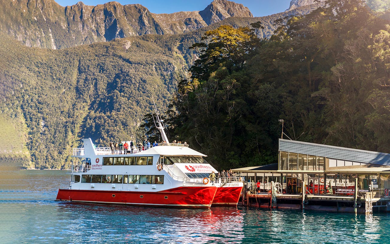 Cruise boat docked at Milford Sound with scenic mountain backdrop, Te Anau tour.