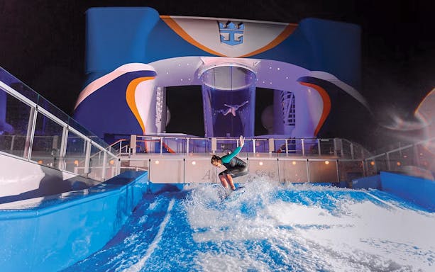 Surfer riding wave on cruise ship's surfboarding area at night.