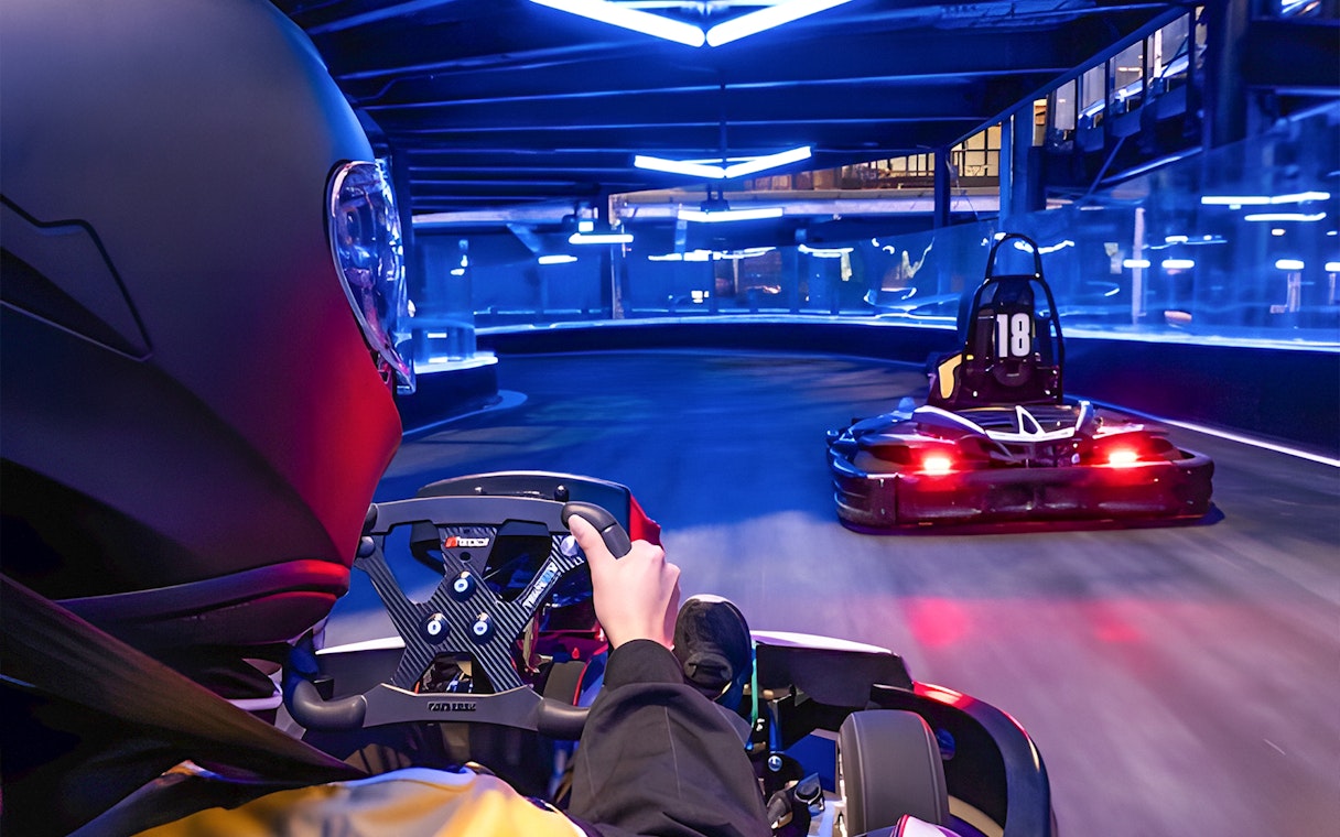 Go-kart racing on an indoor track with neon lights, part of Combo: HyperDrive and UltraGolf experience.