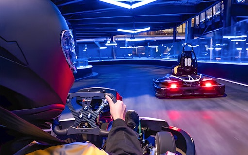 Go-kart racing on an indoor track with neon lights, part of Combo: HyperDrive and UltraGolf experience.