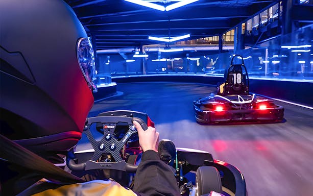 Go-kart racing on an indoor track with neon lights, part of Combo: HyperDrive and UltraGolf experience.