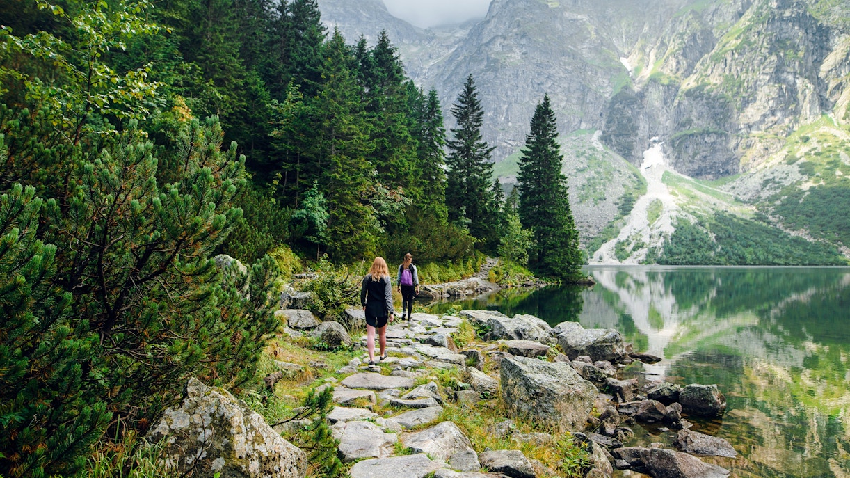 Women hiking along Morskie Oko lake trail, surrounded by mountains in Zakopane, Poland.