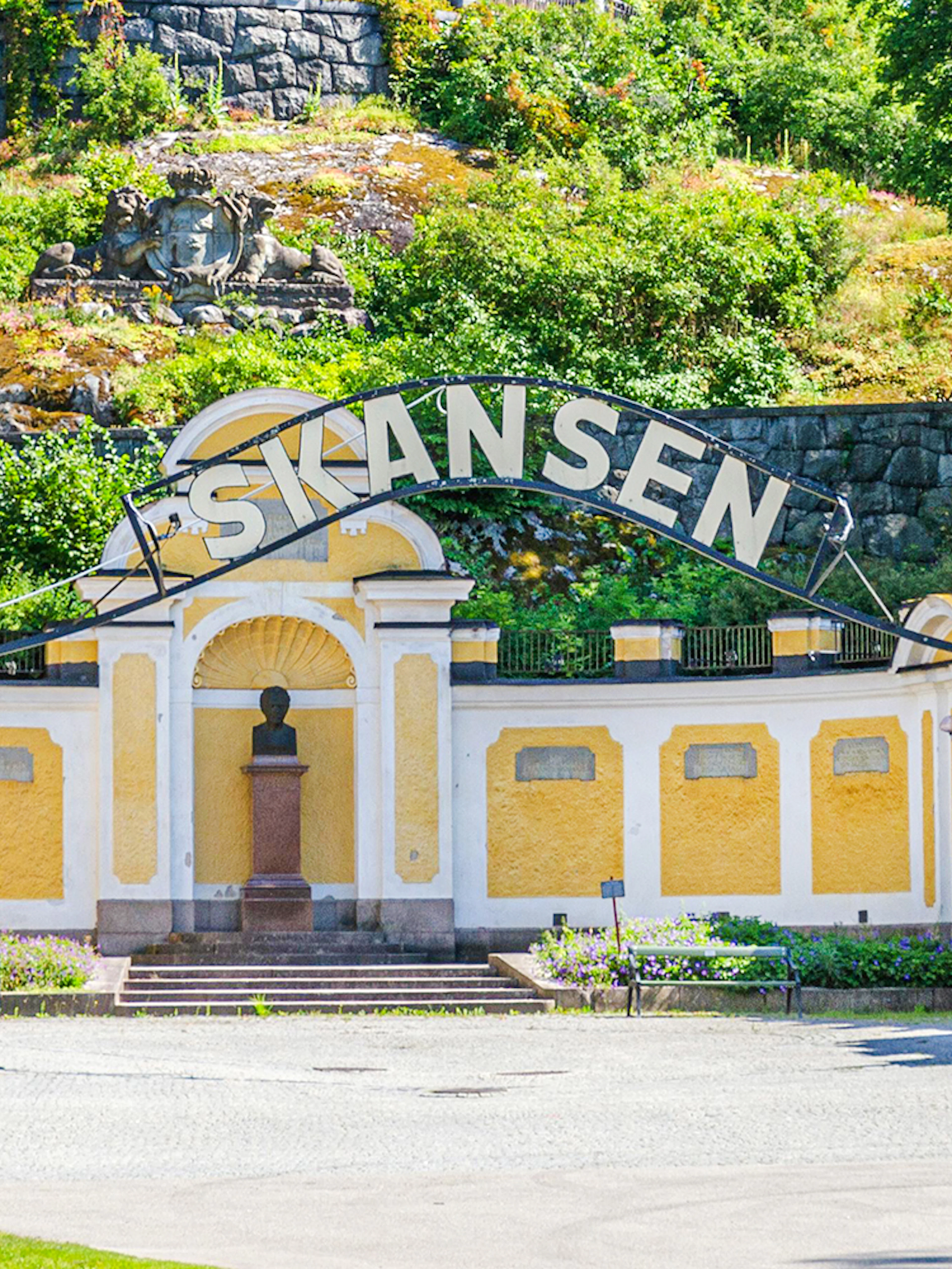 Exterior entrance of Skansen open-air museum in Stockholm, Sweden, with yellow buildings and greenery.