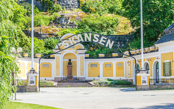 Exterior entrance of Skansen open-air museum in Stockholm, Sweden, with yellow buildings and greenery.