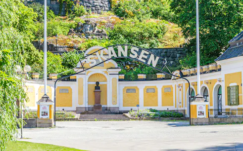 Exterior entrance of Skansen open-air museum in Stockholm, Sweden, with yellow buildings and greenery.