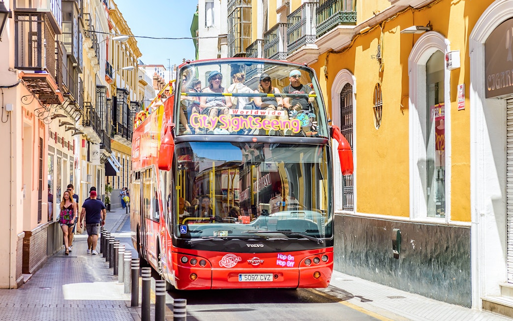 City Sightseeing Hop on Hop off bus navigating a narrow street in Seville.