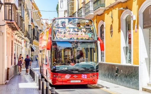 City Sightseeing Hop on Hop off bus navigating a narrow street in Seville.