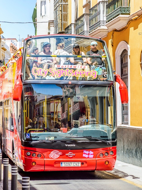 City Sightseeing Hop on Hop off bus navigating a narrow street in Seville.