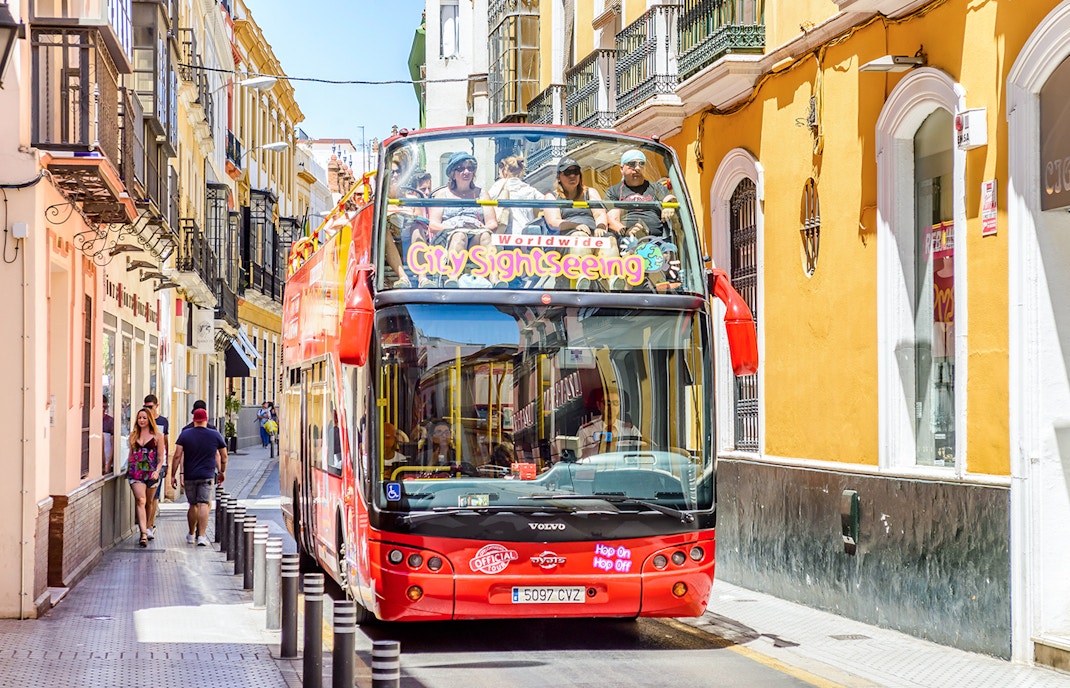 City Sightseeing Hop on Hop off bus navigating a narrow street in Seville.
