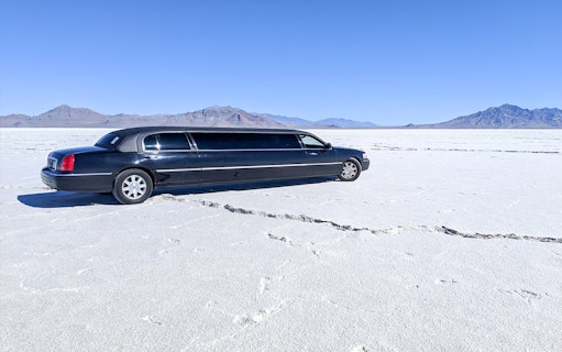 Limousine parked on a vast salt flat with mountains in the background.