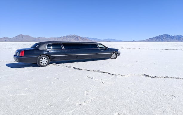 Limousine parked on a vast salt flat with mountains in the background.