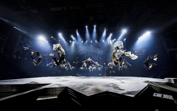 Performers leaping with newspapers in a dramatic scene from Newsies musical.