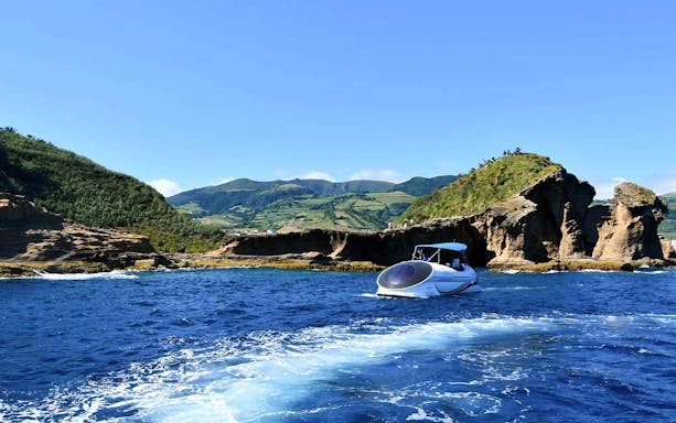 Glass bottom boat on São Miguel's blue waters near rocky coastline.