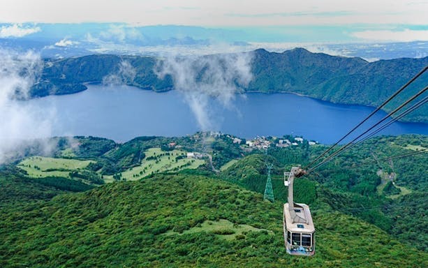 Hakone Komagatake Ropeway ascending over lush green mountains with Lake Ashi in the background, Japan.