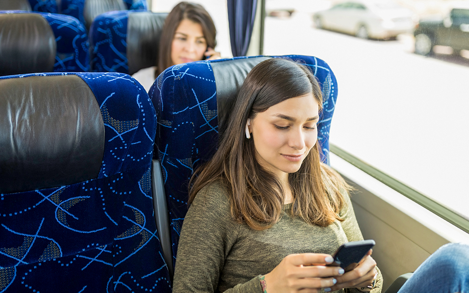 Guests relaxing on AC coach bus using mobile devices.
