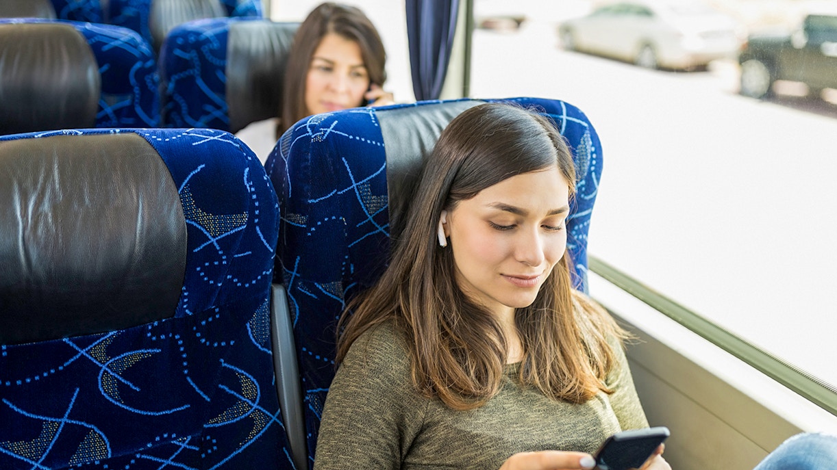 Guests relaxing on AC coach bus using mobile devices.
