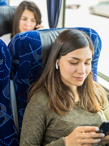Guests relaxing on AC coach bus using mobile devices.