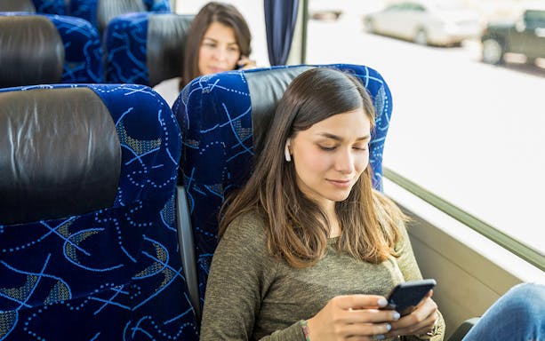 Guests relaxing on AC coach bus using mobile devices.