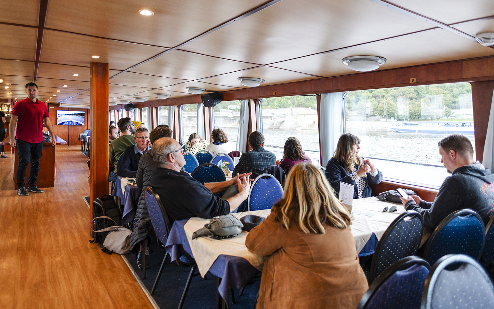 Tourists enjoying a sightseeing cruise inside a boat on the Vltava River in Prague.