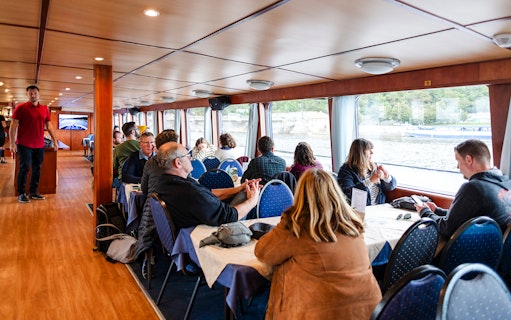 Tourists enjoying a sightseeing cruise inside a boat on the Vltava River in Prague.