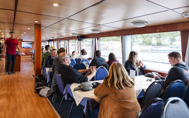 Tourists enjoying a sightseeing cruise inside a boat on the Vltava River in Prague.