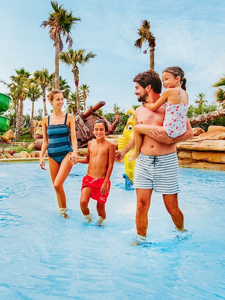 Family enjoying water play at Caribe Aquatic Park with slides and palm trees.