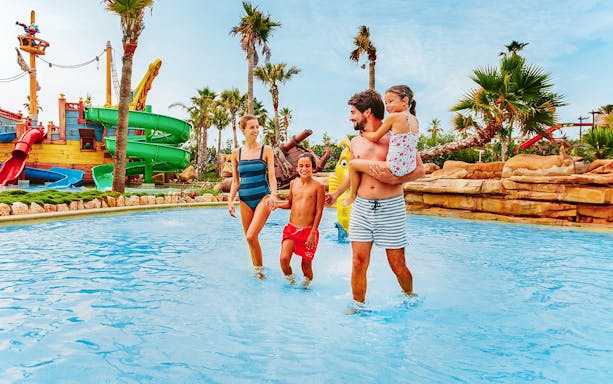 Family enjoying water play at Caribe Aquatic Park with slides and palm trees.
