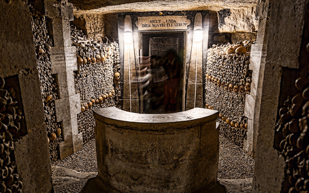 Underground catacombs with walls lined with human skulls and bones.