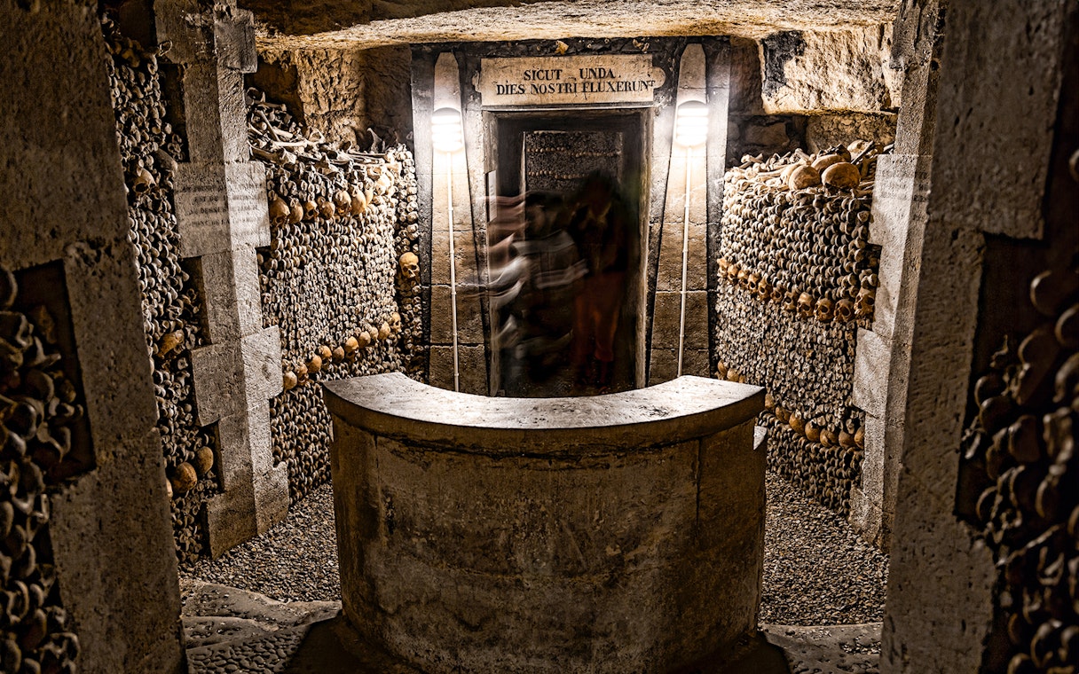 Underground catacombs with walls lined with human skulls and bones.