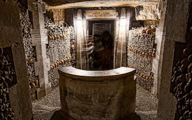 Underground catacombs with walls lined with human skulls and bones.
