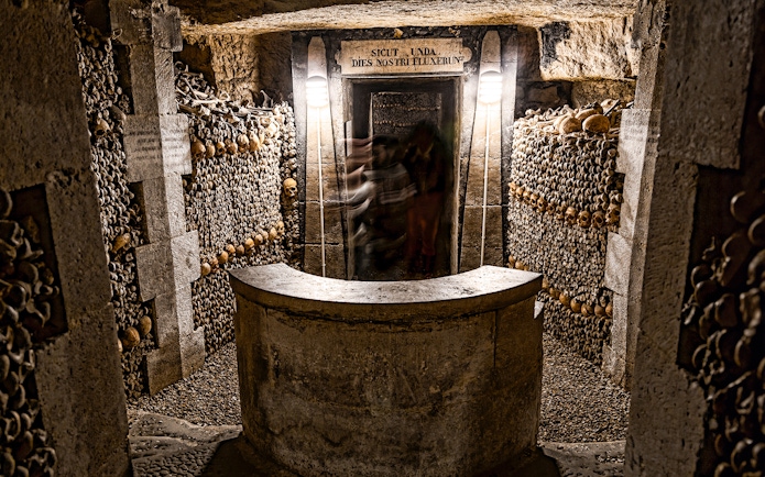 Underground catacombs with walls lined with human skulls and bones.